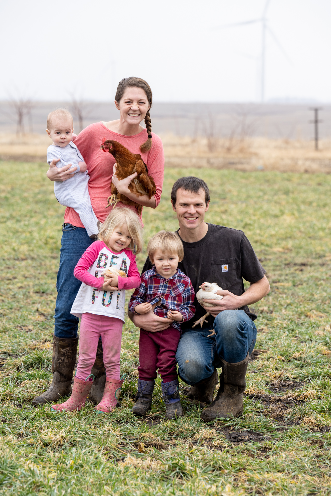 A family of 2 adults and 3 children pose for an image while holding chickens