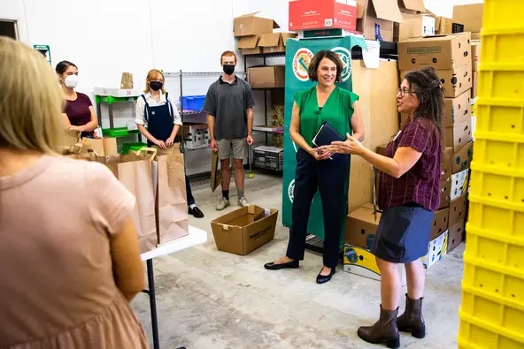 A handful of folks stand in a circle in to Field to Family warehouse surrounded by fruit and vegetable boxes.