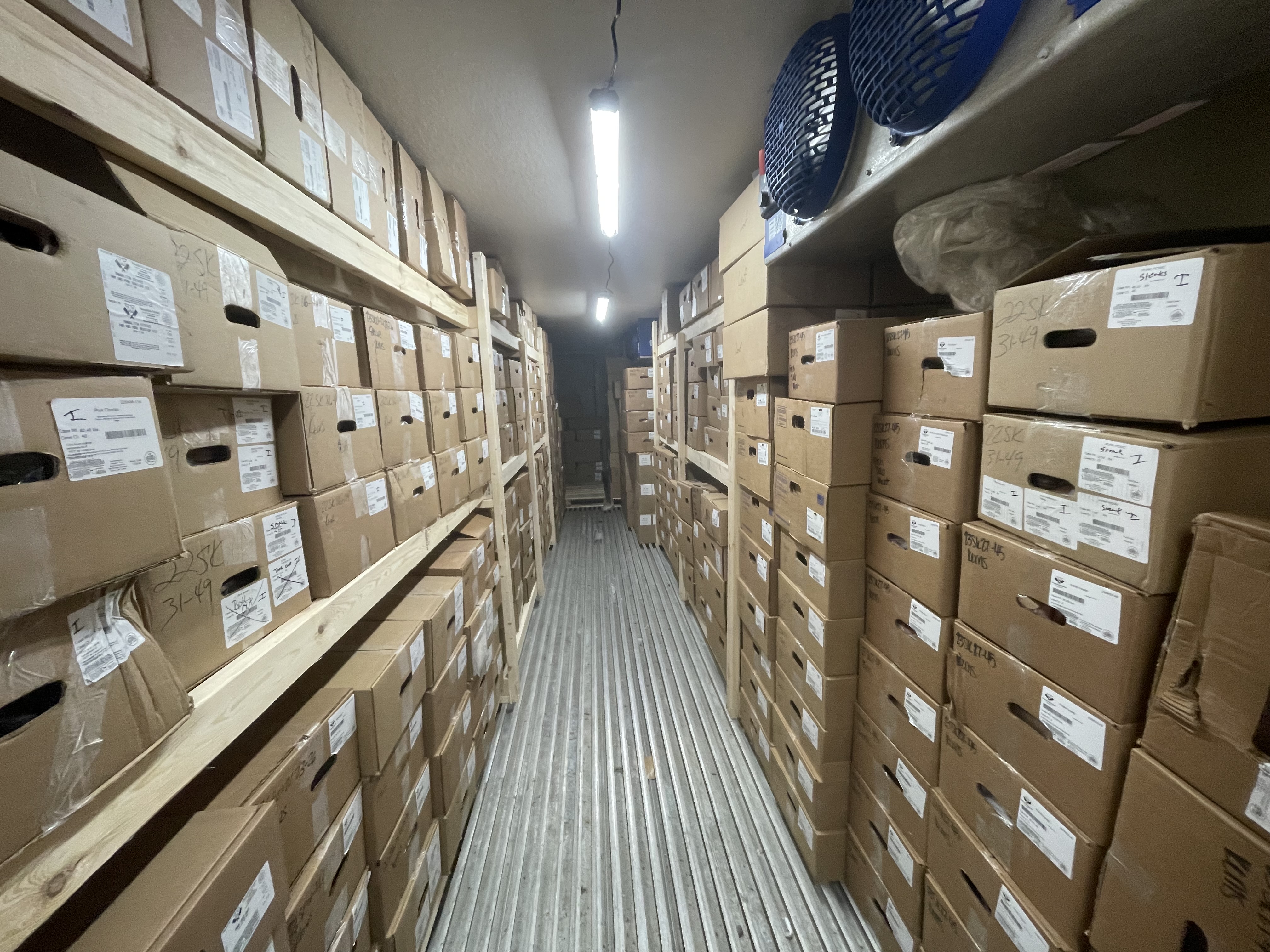 The new freezer has rows of boxes stored on wooden shelves.