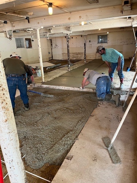 Three men work to lay concrete for new working space.