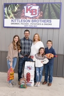 A family of 5 pose with bags of potatoes.