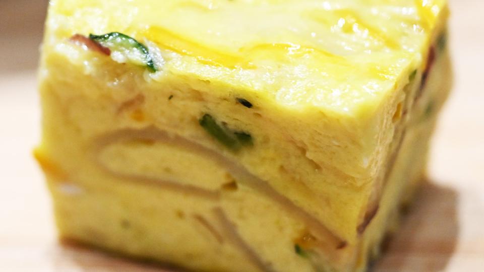 A slice of frittata sits with yellow eggs and slices of vegetables suspended throughout.