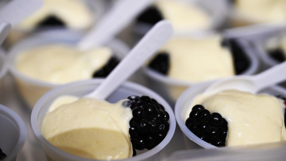 Small servings of cream colored chantilly are served with a little spoon and a blackberry.