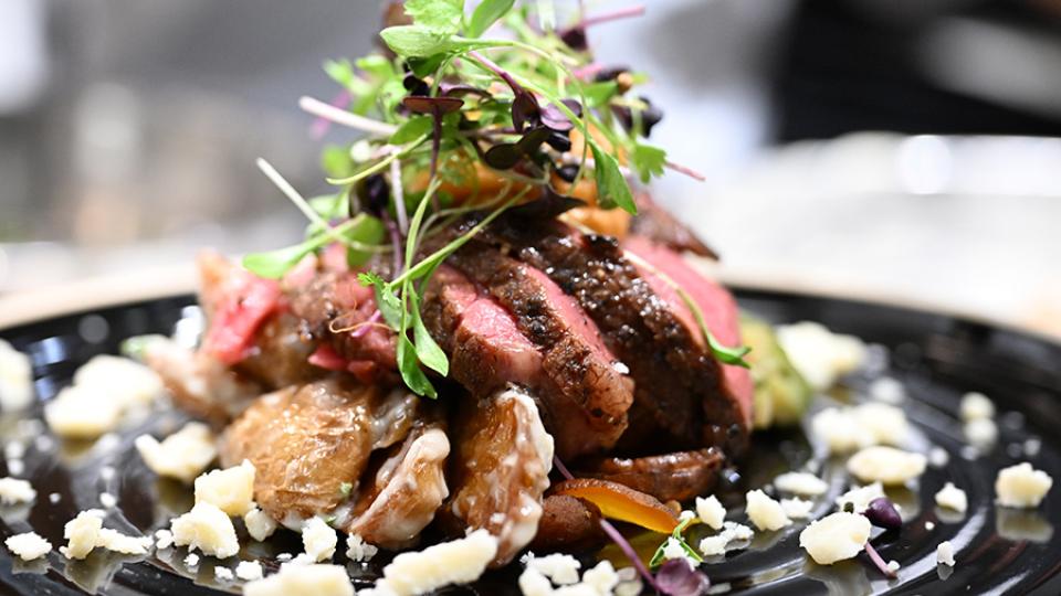 Steaks sits on a bed of beets and fingerling potatoes.  It is topped with pumpkin butter and micro greens.