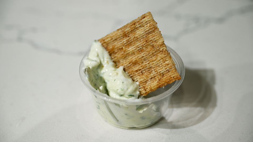 A cracker in a small cup is covered with a green cucumber/pickle dip.