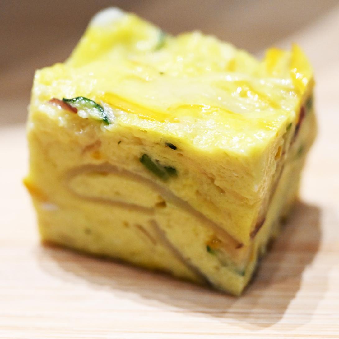 A slice of frittata sits with yellow eggs and slices of vegetables suspended throughout.