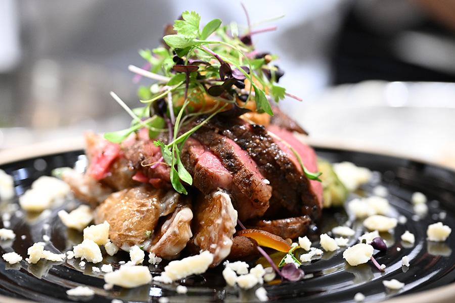 Steaks sits on a bed of beets and fingerling potatoes.  It is topped with pumpkin butter and micro greens.